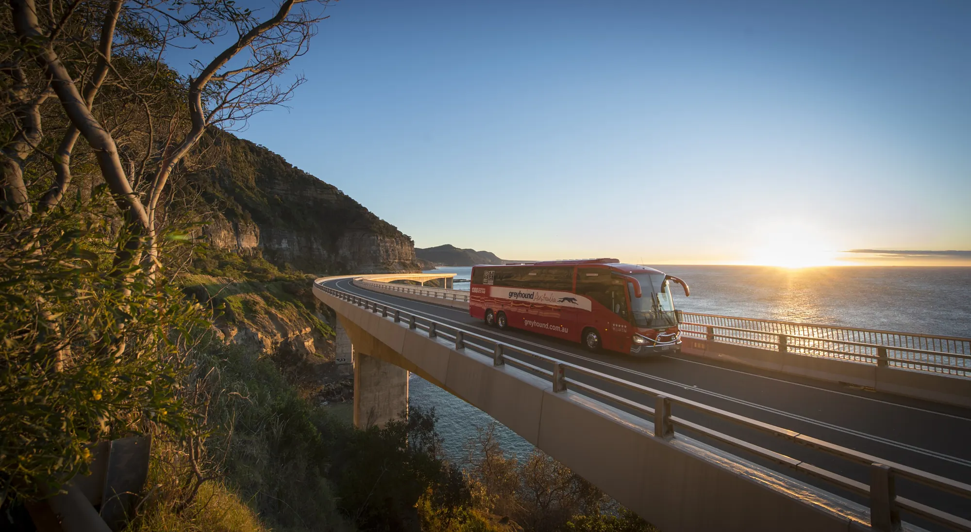 Ein Greyhound-Bus überquert die Sea Cliff Bridge bei Sonnenaufgang, NSW