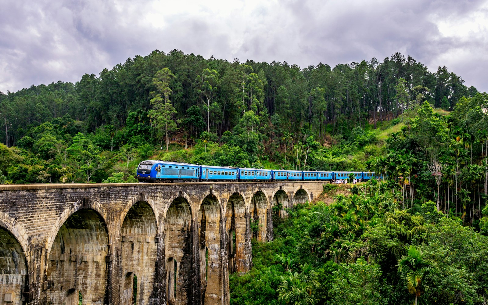 A blue train crossing the Nine Arches Bridge in Sri Lanka's hill country, surrounded by jungle